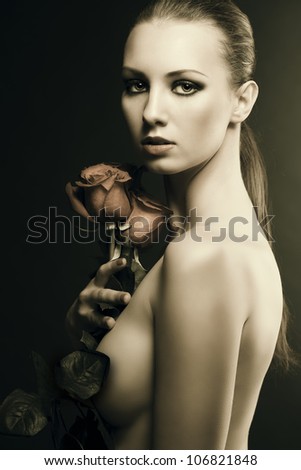 pretty blonde girl\'s low key portrait with three red roses, her body is turned in profile, looks in to the lens and she takes the roses with right hand