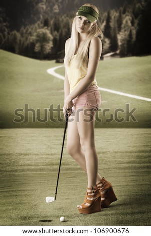 pretty blonde girl\'s playng golf with golf club, pink shorts and green sunshade. she is turned of three quarters at right and looks in to the lens