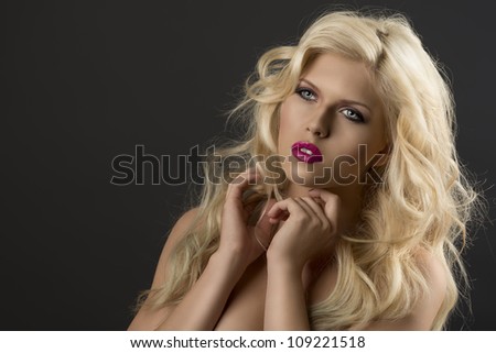portrait of young sexy girl with blode wavy hairstyle and and flying hair from wind, she is turned of three quarters at right and her both hands are near the face