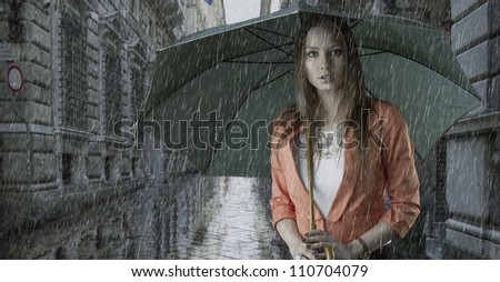 pretty young woman with green umbrella, under the rain falling down in a old fashion street