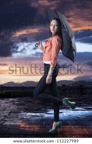 pretty young woman with dark umbrella, her body is turned in profile and she looks in to the lens