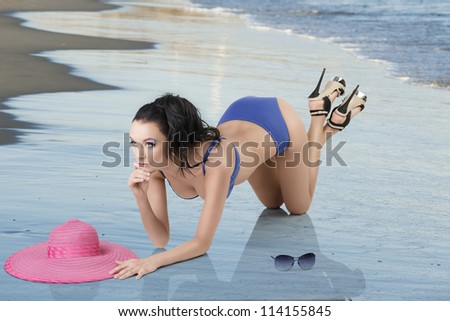 sexy brunette in blue bikini with hat and sunglasses, she is kneeling with elbows on the floor and head on the hand