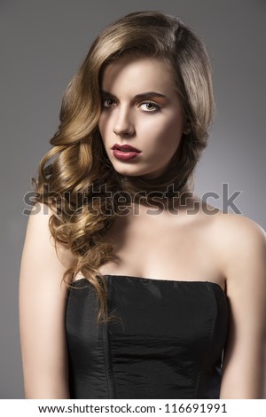 beautiful woman with long wavy hair and dark dress, her face is turned of three quarters at right and looks in to the lens