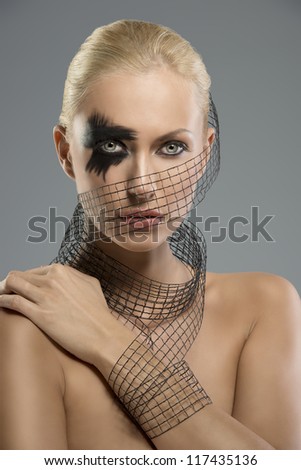 Pretty blonde girl with dark make-up and grid around the neck, the face and wrist, she looks in to the lens and her left hand is on the right shoulder