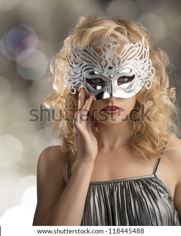 pretty blonde girl with curly hair takes one silver mask, she is in front of the camera and takes the mask on the face with right hand