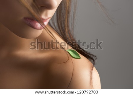 close-up portrait of woman with naked shoulder with leaf and part of the face behind flying hair