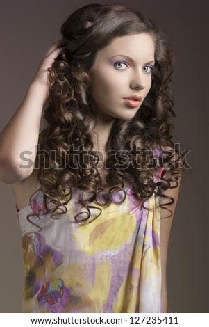 young and pretty lady with curly hair wearing a floral colorful dress on dark brown background