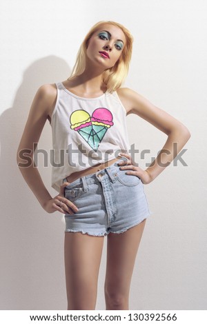 young nice blonde female in summer time wearing tank, sexy denim shorts posing near white wall