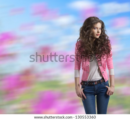 very nice young girl brunette with wavy and volume hair wears blue jeans and pink jacket, colorful background