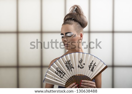 sexy brunette with japan make-up and asian fan, her face is turned at right and she looks down