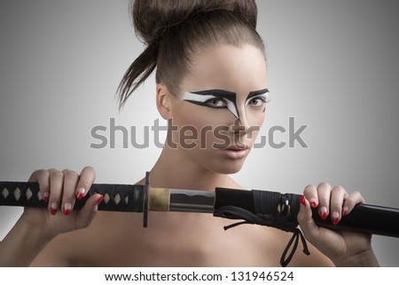 pretty brunette with japan make-up japan sword, her face is turned of three quarters at left and she takes the sword with both hands