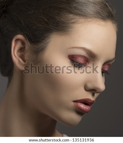 close-up portrait of brunette female with red glossy make-up turned of three quarters on gray background