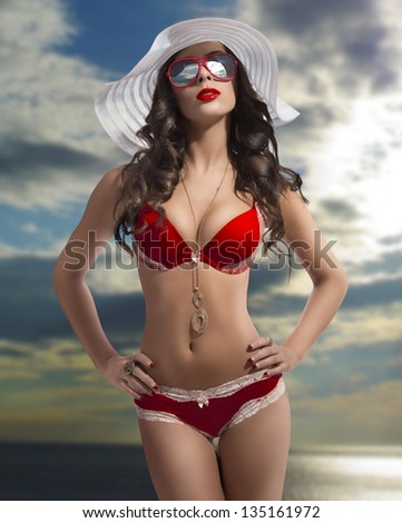 brunette woman with very sexy bikini, big sunglasses and summer white hat with cloudy sky background