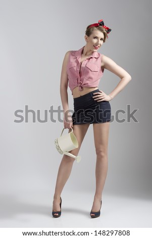 portrait of blonde woman gardener wearing  like sexy pin-up with short skirt, heels and watering can in the hand