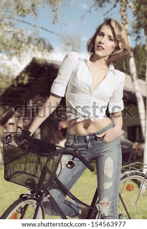portrait of pretty blonde girl with casual style wearing jeans and white shirt  posing on a bicycle in summertime