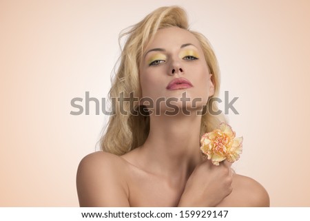 close-up portrait of sexy blonde woman with colorful make-up and naked shoulders taking in the hand one carnation