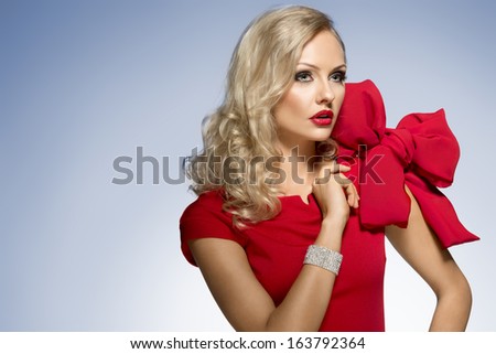 beautiful blond woman in red dress with nice hair style and a big bow on shoulder. she looks somewhere with surprise expression