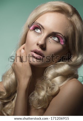 close-up shoot of sexy blonde girl with nice long wavy hair and pink feathered creative make-up looking up with romantic expression