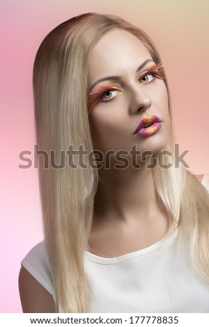 cute blonde girl with creative colorful make-up and feathered eyelashes, long silky smooth hair and white dress
