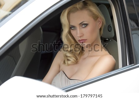 sensual blonde girl with elegant dress and cute make-up sitting in a white car and looking in camera