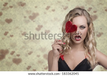 very pretty blonde female taking heart shaped lollipop in the hand, posing with long wavy hair and sexy dress