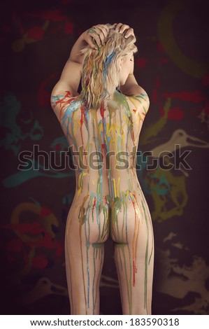 sensual blond girl naked with some color paint running on her body on black background