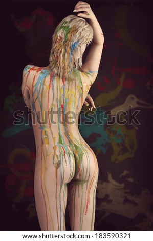 beautiful blond nude girl with multicolored body paint over her body giving sexy pose against gray background.