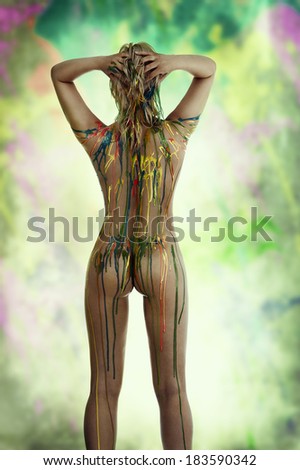 beautiful blond nude girl with multicolored body paint over her body giving sexy pose from back view against white background.