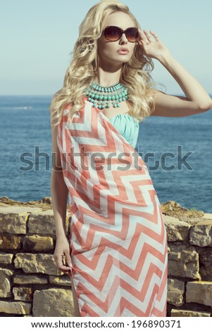 fashion blonde female in vacation. Posing with cute summer style, pareo on bikini, sunglasses and big turquoise neckalce