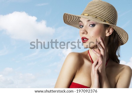 Young girl in a hat is holding her hand near face , and wearing a summer hat on blue light sky