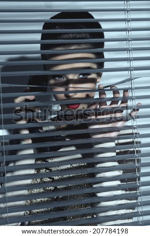 sexy spy woman with vintage style talking on the phone, taking retro receiver near face behind closed shutters of window