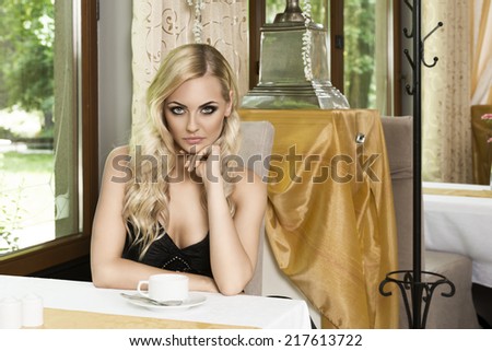 stunning woman in old fashion restaurant , sitting at table and looking in camera . she has cup of tea
