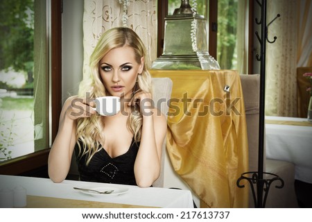 cute girl sitting at table in old fashion bar , looking in camera in act to drink a cup of tea