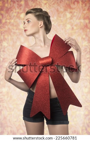 christmas shoot of sensual young girl with elegant hair-style, colorful make-up and big red bow on her beast, adorned like a present