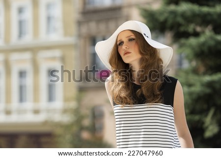 Beautiful woman in white summer hat. She has curly, long, brown hair. Her makeup is so soft. She wears striped dress.