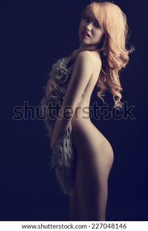 Sexy, nude woman with ginger hair cover her body with fluffy fur. She has got nice makeup and beautiful jewellery.