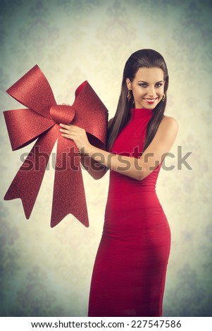 pretty girl with long brown hair  posing in christmas concept shoot with red dress and big red bow, smiling and looking in camera