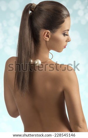 sexy brunette woman turned on her naked back posing with stylish make-up, ponytail hair-style and golden accessory