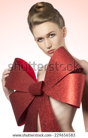 close-up christmas shoot of naked girl with elegant hair-style and big glitter red bow on her breast