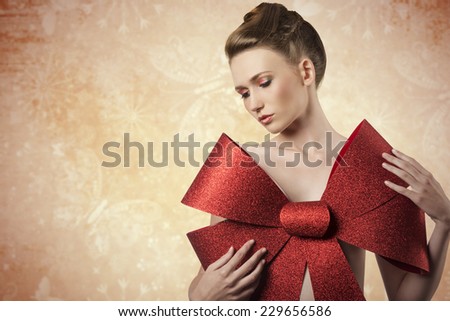 christmas shoot of sensual young girl adorned like a present  with elegant hair-style, colorful make-up and big red glitter bow on her beast,