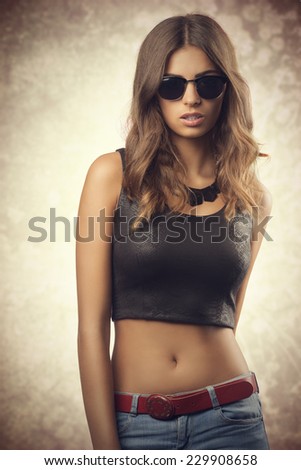 Beautiful, confident, young woman with sunglasses. She wear black top, jeans. She has got brown, curly hair.