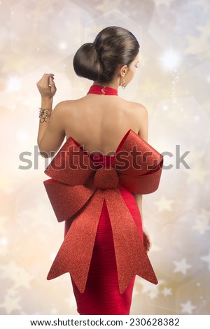 sexy brunette woman posing turned on her back with red christmas dress, big glitter bow and golden jewellery
