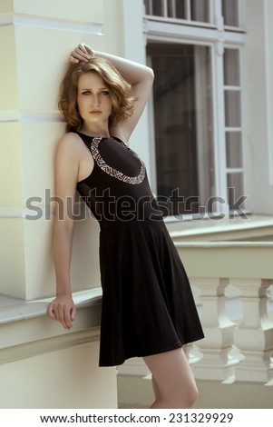 fashion shoot of pretty young girl with natural hair-style wearing stylish black dress and posing outdoor near building
