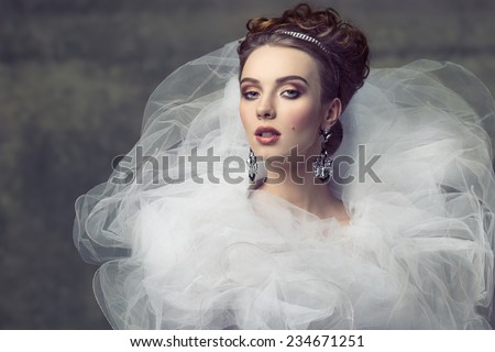 cute young girl wearing like sophisticated dame with creative romantic dress, elegant hair-style, shiny tiara, precious earrings and stylish make-up. Looking in camera with arrogant expression