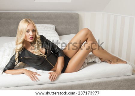indoor glamour portrait of provocative  blonde girl with dark lingerie and leather jacket, lying on bed looking in camera with erotic expression
