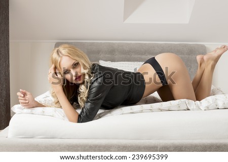 charming blonde lady posing in allure pose on bed, wearing leather jacket and black panties and looking in camera. Erotic shoot