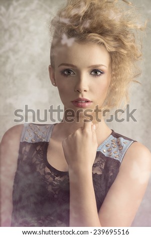Young, pretty girl with blonde wild hair is wearing transparent black blouse with denim parts. She has got colorful make up .