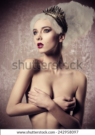 artistic fashion portrait of nude sensual woman with creative baroque hairdo and golden accessories on the head posing with stunning make-up and covering her breast.
