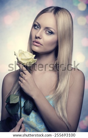 sensual blonde lady with silky long hair posing with white rose in the hand s and wearing stylish spring dress