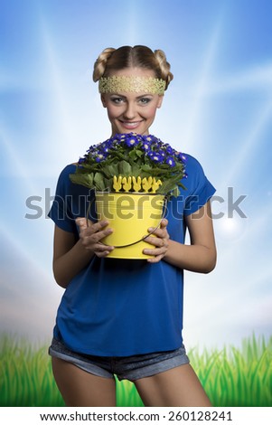 Pretty, fresh, natural woman with blonde short hairstyle with little decorations, wearing blue t-shirt and holding little blue flowers.